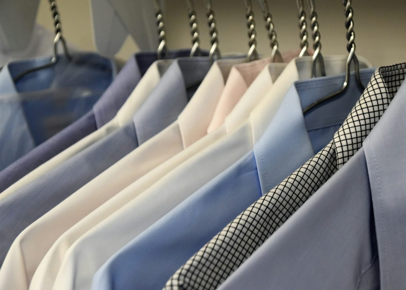 A row of freshly pressed shirts on hangers in soft blues and whites